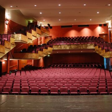 Der Theatersaal mit Sitzreihen im Parkett, auf der Empore und den Balkonen. Davor teilweise Bühnenboden