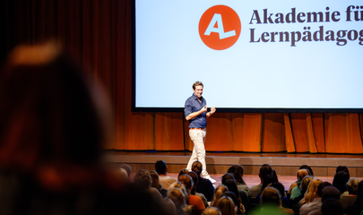 Dozent der Akademie für Lernpädagogik auf der Bühne, führt zum Kalendereintrag