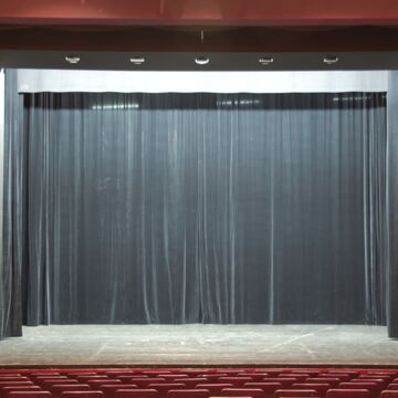 Theaterbühne mit gescholssenem, schwarzen Vorhang davor Sitzreihen