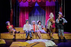 6 SchauspielerInnen in schrillen Kostümen im bunten Bühnenbild stehend und sitzend