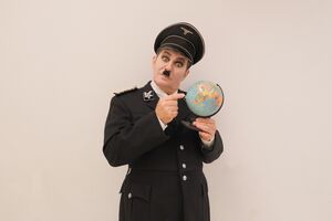 Andreas Guglielmetti als der große Diktator in Uniform mit Globus in der Hand, führt zum Kalendereintrag